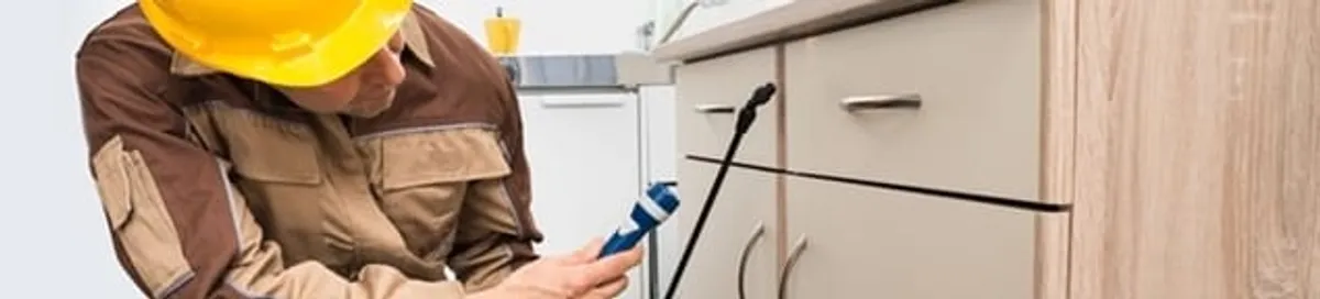 Roach exterminator applying treatment under kitchen cabinets in Lakewood, CO