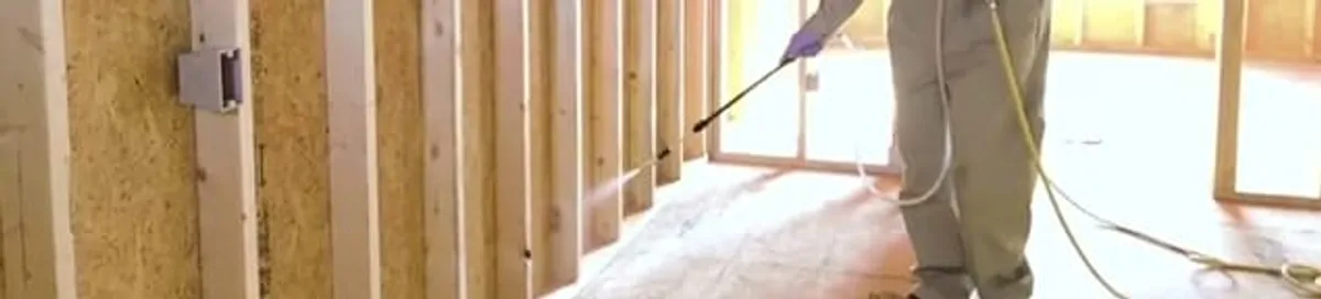Termite treatment technician applying spray along framing and unfinished walls in Lakewood, CO
